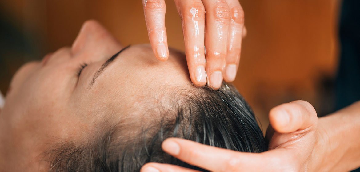 Frau bekommt eine Kopfmassage mit Öl gegen Haarausfall